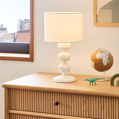 a lamp that is sitting on top of a dresser next to a small toy dinosaur