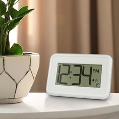 a white clock sitting on top of a table next to a potted green plant