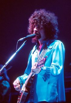 a man that is standing up in front of a microphone and holding a guitar on stage