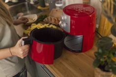 a woman standing in front of a red pot on top of a counter