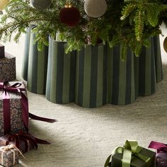 presents under a christmas tree with ornaments and ribbons on the ground next to it,