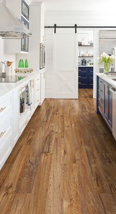 an open kitchen with white cabinets and wood flooring, along with a large wooden door leading to the dining room