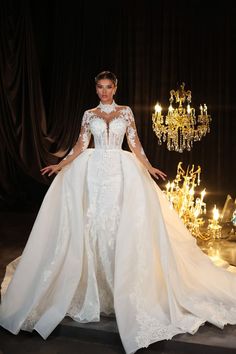 a woman in a white wedding dress standing next to a chandelier with lights on it