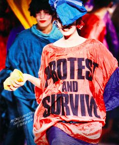 a woman walking down a runway wearing a red shirt and blue pants with words written on it