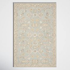 a blue rug with an ornate design on the bottom and beige trimmings, in front of a white wall