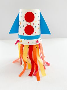 a paper rocket ship with streamers and confetti on the bottom, sitting on a white surface