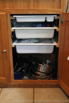 the kitchen cabinet is open to reveal several containers and pans in it's bottom drawer