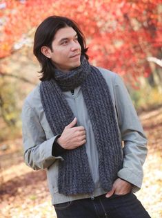 a man standing in the woods wearing a knitted scarf and jacket with his hands on his hips