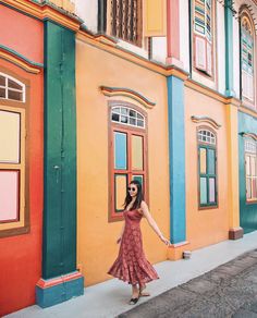 a woman in a red dress is standing by some colorful buildings and holding her hand out