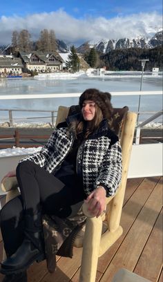 a woman sitting in a chair on top of a wooden deck next to a body of water