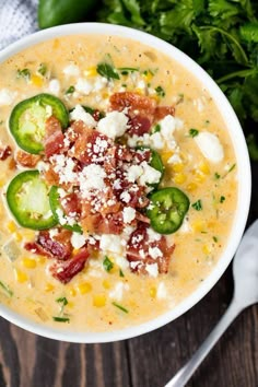 a close up of a bowl of soup with cheese and vegetables on the side next to a spoon