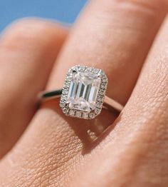 a woman's hand holding an engagement ring with a large emerald stone in the center