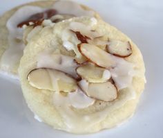 two cookies with white icing and almonds on top are sitting on a plate