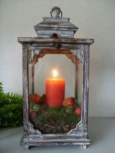 a candle is lit in an old lantern with moss and pine cones on the table