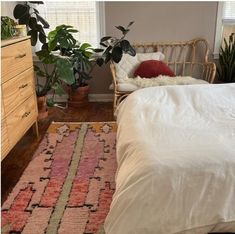 a bed sitting next to a wooden dresser in a room with plants on top of it