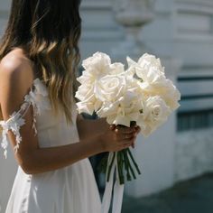 a woman in a white dress holding a bouquet of flowers with her back to the camera