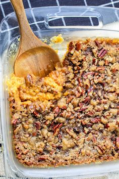 a casserole dish filled with sweet potatoes and crumbled pecans, topped with a wooden spoon