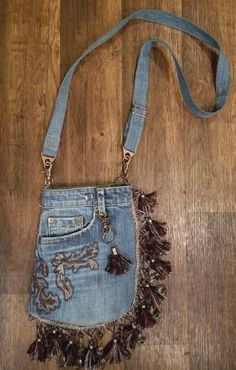 a denim purse with tassels hanging from it's side on a wooden floor