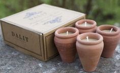 four clay pots sitting on top of a rock next to a box filled with candles