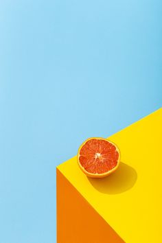 an orange slice sitting on top of a yellow and blue block against a blue sky