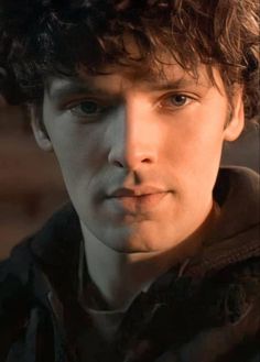 a close up of a person with curly hair wearing a jacket and looking at the camera