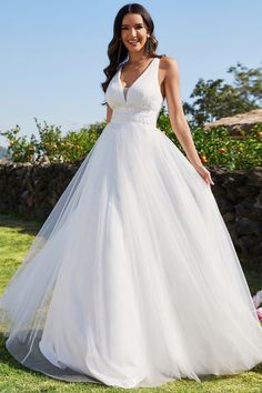 a woman in a white wedding dress standing on the grass with her arms behind her back