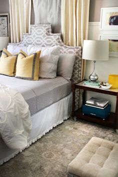 a bed with white and yellow pillows on top of it next to a night stand