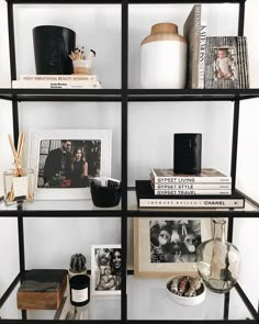 the shelves are filled with books, pictures and other items in black metal frames on white walls