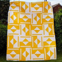 a yellow and white quilt hanging on a clothes line in front of some bushes,