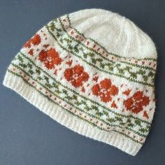 a white knitted hat with red flowers on the front and green, orange, and yellow trim