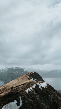 two people standing on top of a snow covered mountain next to a body of water