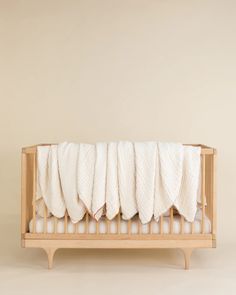 a wooden crib with white sheets on it and a beige wall in the background