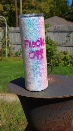 a pink and blue glitter tumbler sitting on top of a metal object in the grass