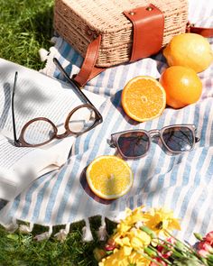 an open book, sunglasses and oranges on a blanket in the grass near flowers