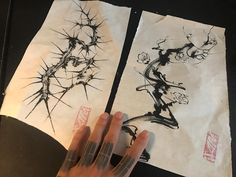 two pieces of paper that have been drawn with ink and are being held by someone's hand