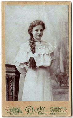 an old black and white photo of a woman in a dress with a long braid