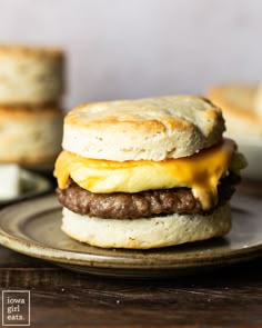 an egg and cheese breakfast sandwich is on a plate with biscuits in the background