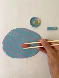 a person holding two chopsticks in front of a painting