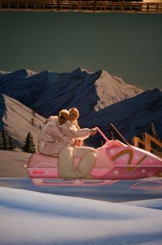 two people riding on a pink sled in the snow with mountains in the background