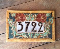 a house number plate with flowers on it sitting on a wooden floor next to a wall