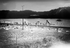 an old black and white photo of people swimming in the water at a beach with mountains in the background