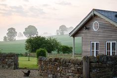 a dog is standing in front of a stone fence and house on a foggy day