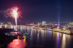 fireworks are lit up in the night sky over a river and cityscape with lights on it