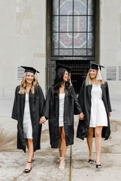 three women in graduation gowns and caps are standing outside the building with their hands in each other's pockets