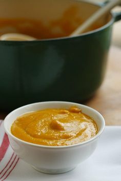 a white bowl filled with orange sauce next to a green pan on a wooden table