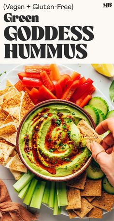 a person dipping guacamole into a bowl surrounded by vegetables and tortilla chips