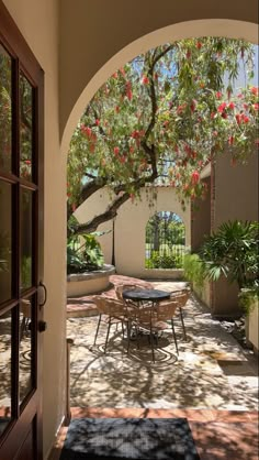 an archway leading to a patio with tables and chairs under a tree in the shade