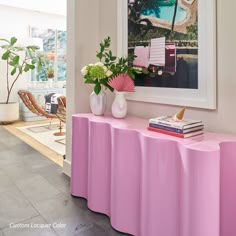 a pink table with vases and flowers on it in front of a large painting