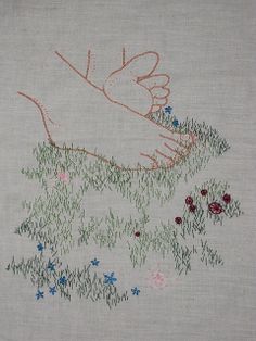 the embroidery on this piece shows two hands touching each other's fingers, with flowers and grass in the foreground