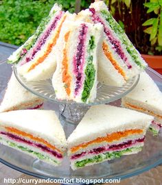 there are many small sandwiches on the glass platter with one cut in half to show it's colors